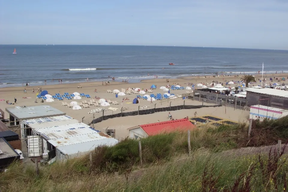 Strandtenten en een druk strand gezien vanaf het duin met de zee erachter
