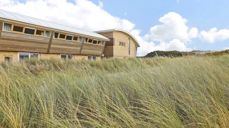 Appartementengebouw met golvend dak achter het helmgras in de duinen