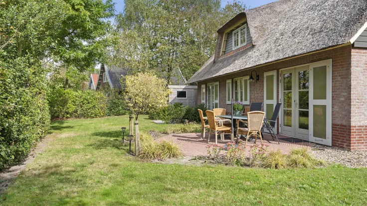 Rietgedekte villa met terras, tuinset en een gazon met leibomen