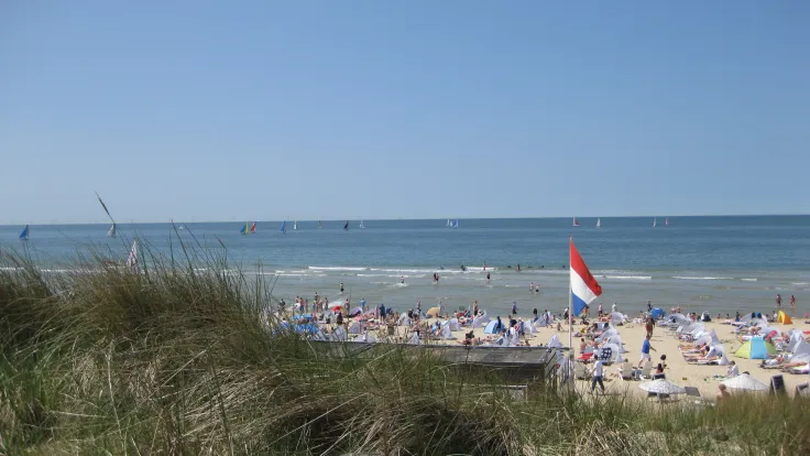 Uitzicht vanaf het duin met helmgras over een druk strand met een vlag