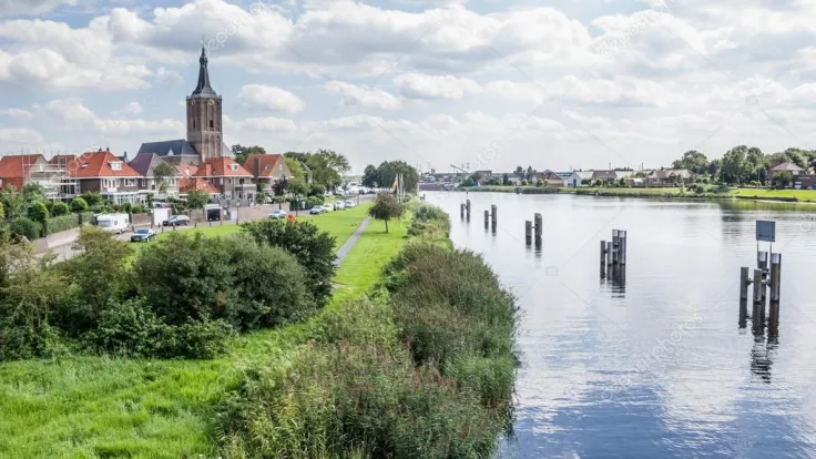 Dorp met kerktoren aan de oever van een rivier met groene bermen