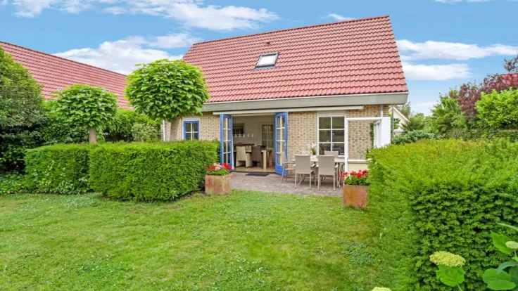 Vakantiewoning met rood dak en terras achter een hoge haag en hortensias