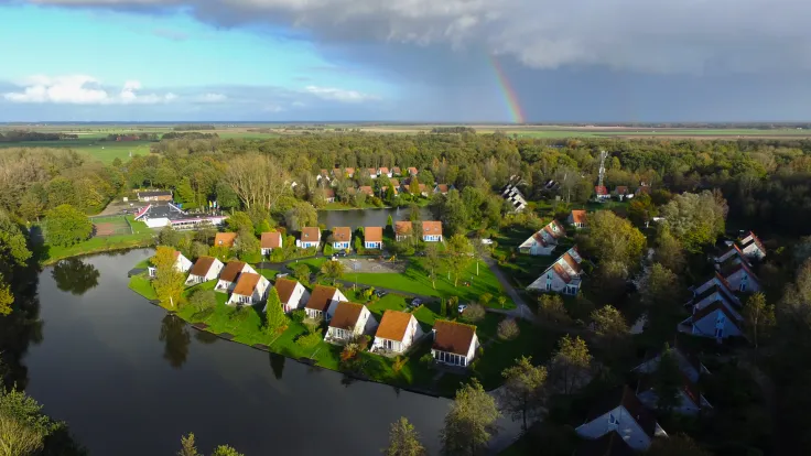 Luchtfoto van het vakantiepark met woningen langs het water en een regenboog